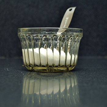 Twelve teaspoons of sugar and a metal teaspoon in glass bowl.