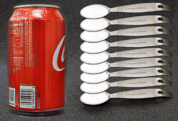 Can of soda and 9 individual teaspoons of sugar.