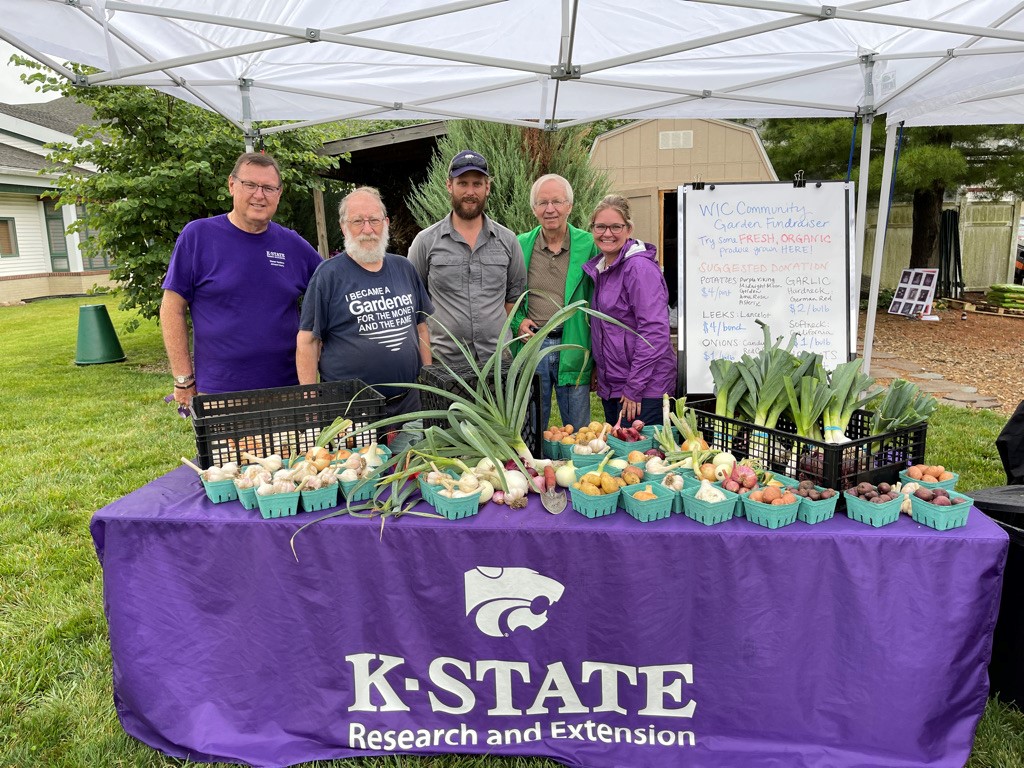 four people standing together behind a table of vegetables