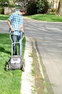 Grass clippings swept down gutter by water as mower watches