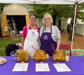 Two women serve food behind Table